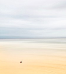 Two men walking on sand before the rising tide
