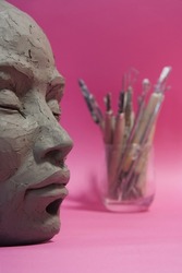 Clay sculpture with tools. Female face on pink background. Creation process. Arts and crafts.