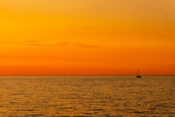 Orange and yellow sunset on the sea with a sailboat. Minimalistic photo of a silhouette of sailing boat on the sea during dusk.