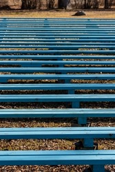Vertical photo of bright blue benches at park at sunny day during early spring. Construction of wooden benches. Blue urban lines and patterns outdoor. Weathered open-air stage pews. 