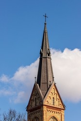 Dark yellow stone church spire at white cloud and blue sky background. Torņakalns Church steeple spire at Riga, Latvia. Vertical photo of Lutheran church bell tower at early spring.