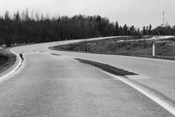 Monochromate photo of curvy asphalt road at cloudy early spring day. Black and white fixed countryside small street at Latvia. Monochromatic tarmac road with curves.