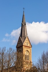 Dark yellow stone cathedral spire at white cloud and blue sky background. Torņakalns Church bell tower spire at Riga, Latvia. Vertical photo of Lutheran church steeple at early spring.