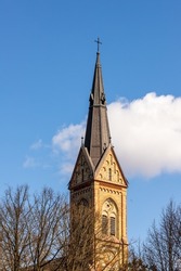 European stone cathedral spire at white cloud and blue sky background at early spring. Torņakalns Church tower at Riga, Latvia. Vertical photo of Lutheran church steeple at sunny day.