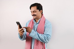 Beautiful portrait of an happy Indian bearded farmer man in rural India concept. Funky expressions white background. Cheerful farmer looking into the mobile phone screen and using technology.