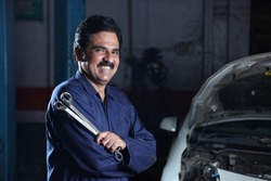 Portrait of a happy car mechanic in moustache standing beside a car in service station. Car Specialist is holding car repairing tools. Professional repairman is smiling in modern clean work workshop.