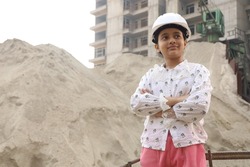 Aspirational Indian female child engineer standing on a construction site. Confident girl standing wearing a construction helmet.