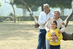 Grand parents enjoying with the grand daughter in the park surrounded with greenery and serenity. They are having a joyful and cheerful time together in lush green environment.