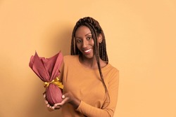 happy black young woman celebrating easter egg gift in beige studio background. holiday, easter, celebration concept.