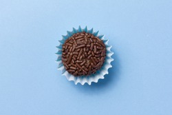 Brigadeiro is a typical homemade chocolate truffle from Brazil. Cocoa, condensed milk and sprinkles of chocolate. Common in children birthday party. Top view of candy on blue background.