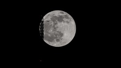 super full moon behind the Stuttgart TV Tower - the antenna is touching the moon. An airplane is flying across