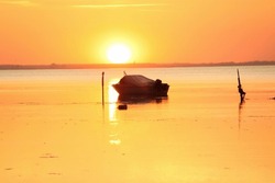 Silhouette of a motor vessel on calm baltic sea during golden sunset. Boat tied to a pole, close to the beach of Greifswald, Germany