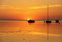 Silhouette of a some motor vessels and sailing boats on calm baltic sea during golden sunset. Boats tied to  poles, close to the beach of Greifswald, Germany