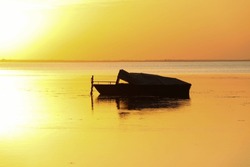 Silhouette of a motor vessel on calm baltic sea during golden sunset. Boat tied to a pole, close to the beach of Greifswald, Germany