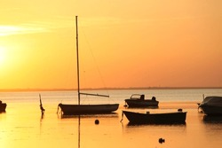 Silhouette of a some motor vessels and sailing boats on calm baltic sea during golden sunset. Boats tied to  poles, close to the beach of Greifswald, Germany