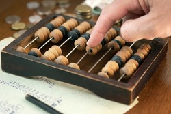 Accountant's hand counting money using vintage wooden abacus with old paper with calculations , pensil and coins lying on the table