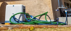 A freshly used, green, water hose is discarded against the wall of a restaurant, on a very sunny and hot day.