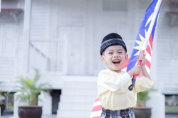 Hari Merdeka Malaysia National Day declared on 31 August every year annually. Boy running happily on green grass field holding Malaysian flag namely Jalur Gemilang
