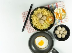 Warm noodles served with eggs and fresh tomatoes with meatballs on a black bowl and pickled on a white bowl and eggs on a white background