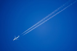 looking up at a twin engine jet airliner in deep blue sky with vapour (contrails) trails diagonally across the frame, KLM Boeing 777-300ER 
