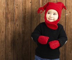 portrait of an adorable kid smiling wearing winter clothes against a wooden background