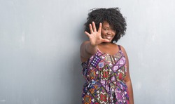 Young african american woman over grey grunge wall wearing colorful dress showing and pointing up with fingers number five while smiling confident and happy.