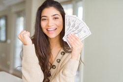 Young woman holding 50 dollars bank notes screaming proud and celebrating victory and success very excited, cheering emotion