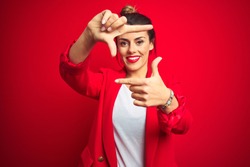 Young beautiful business woman standing over red isolated background smiling making frame with hands and fingers with happy face. Creativity and photography concept.