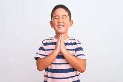 Beautiful kid boy wearing casual striped t-shirt standing over isolated white background begging and praying with hands together with hope expression on face very emotional and worried. Asking