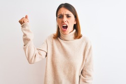 Beautiful redhead woman wearing winter turtleneck sweater over isolated background angry and mad raising fist frustrated and furious while shouting with anger. Rage and aggressive concept.