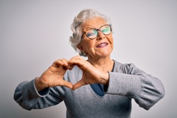 Senior beautiful grey-haired woman wearing casual sweater and glasses over white background smiling in love showing heart symbol and shape with hands. Romantic concept.