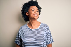 Young beautiful African American afro woman with curly hair wearing striped t-shirt looking away to side with smile on face, natural expression. Laughing confident.