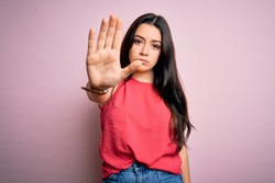 Young brunette woman wearing casual summer shirt over pink isolated background doing stop sing with palm of the hand. Warning expression with negative and serious gesture on the face.