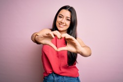 Young brunette woman wearing casual summer shirt over pink isolated background smiling in love doing heart symbol shape with hands. Romantic concept.
