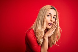 Young beautiful blonde woman wearing casual t-shirt standing over isolated red background hand on mouth telling secret rumor, whispering malicious talk conversation