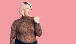 Young blonde plus size woman wearing casual leopard t-shirt smiling with happy face looking and pointing to the side with thumb up. 
