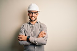 Young architect man wearing builder safety helmet over isolated background happy face smiling with crossed arms looking at the camera. Positive person.