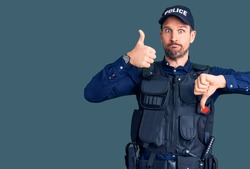 Young handsome man wearing police uniform doing thumbs up and down, disagreement and agreement expression. crazy conflict 
