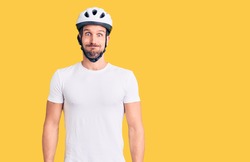 Young handsome man wearing bike helmet puffing cheeks with funny face. mouth inflated with air, crazy expression. 