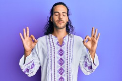 Young handsome man with long hair wearing bohemian and hippie shirt relax and smiling with eyes closed doing meditation gesture with fingers. yoga concept. 