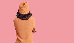 Young beautiful mixed race woman wearing wool sweater and winter hat standing backwards looking away with crossed arms 