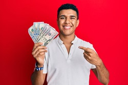 Young arab man holding dollars smiling happy pointing with hand and finger 