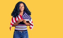 Beautiful african american woman holding united states flag looking positive and happy standing and smiling with a confident smile showing teeth 
