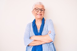 Senior beautiful woman with blue eyes and grey hair wearing casual sweater and scarf happy face smiling with crossed arms looking at the camera. positive person. 