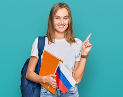 Beautiful young blonde woman exchange student holding russian flag surprised with an idea or question pointing finger with happy face, number one 