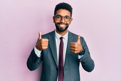 Handsome hispanic business man with beard wearing business suit and tie success sign doing positive gesture with hand, thumbs up smiling and happy. cheerful expression and winner gesture. 