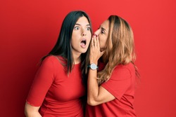 Hispanic family of mother and daughter wearing casual clothes over red background hand on mouth telling secret rumor, whispering malicious talk conversation 
