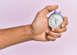 Hand of young hispanic man using stopwatch over isolated pink background.