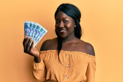 African young woman holding south african 100 rand banknotes looking positive and happy standing and smiling with a confident smile showing teeth 