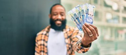 Handsome modern african american man with beard smiling positive standing at the street showing 100 south african rands banknotes